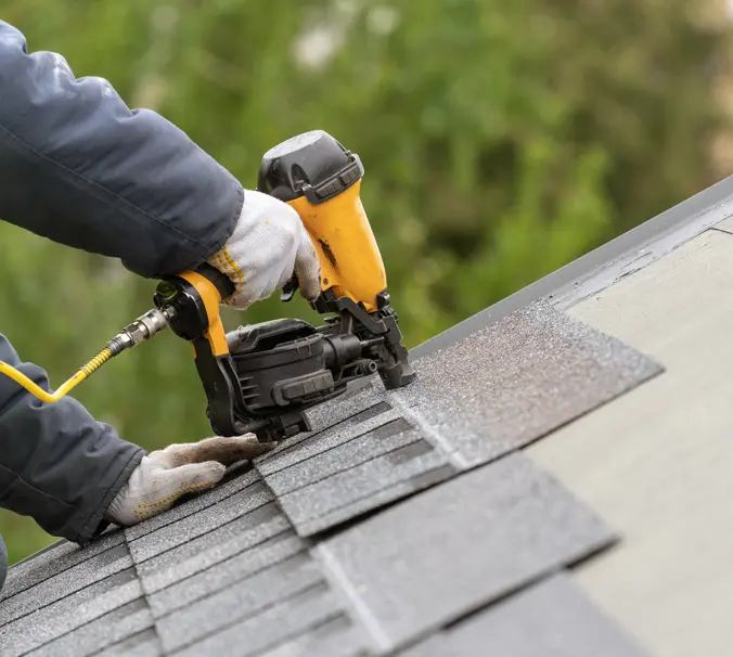 A person is using an electric nail gun to attach shingles.