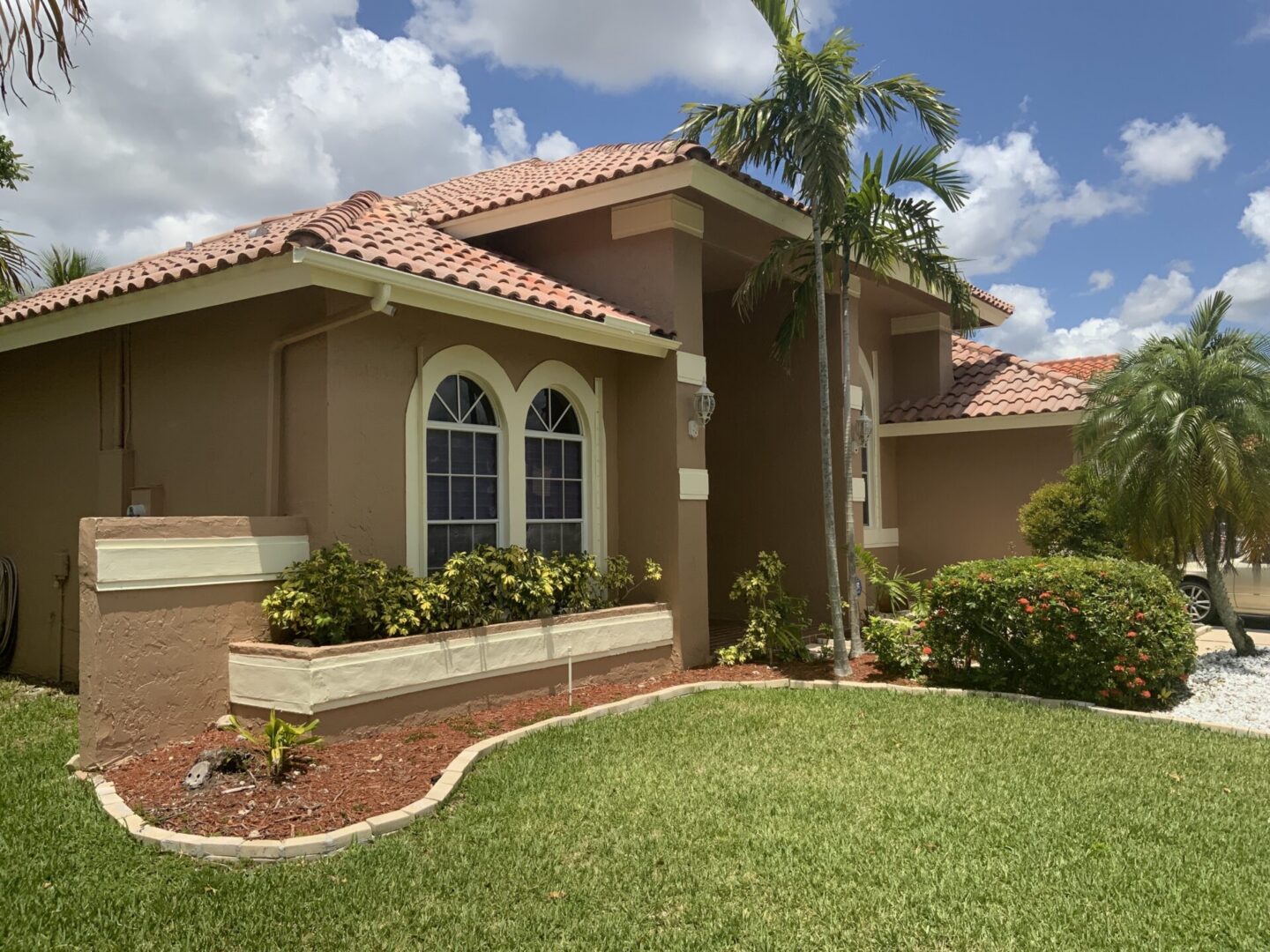 Street-level view of a single-story tan stucco Florida home with a barrel tile roof, arched windows, and landscaped front yard